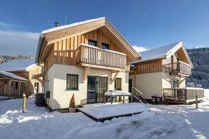 Una cabaña de madera con balcón, un porche cubierto y suelo cubierto de nieve.