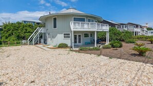 A two-story house with a balcony, a staircase, and a gravel driveway. - Pet Friendly | Ocean Views | Across the Road from the Beach | The Round House (Fernandina Beach)