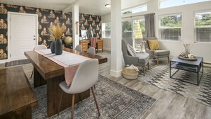 Ein geräumiges Wohnzimmer mit einem großen Esstisch aus Holz, bequemen Sitzmöglichkeiten und Blick ins Freie.
