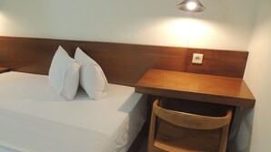 A hotel room with a bed, two pillows, a wooden nightstand, and a chair. - Wisma Tamu UKSW (Salatiga)