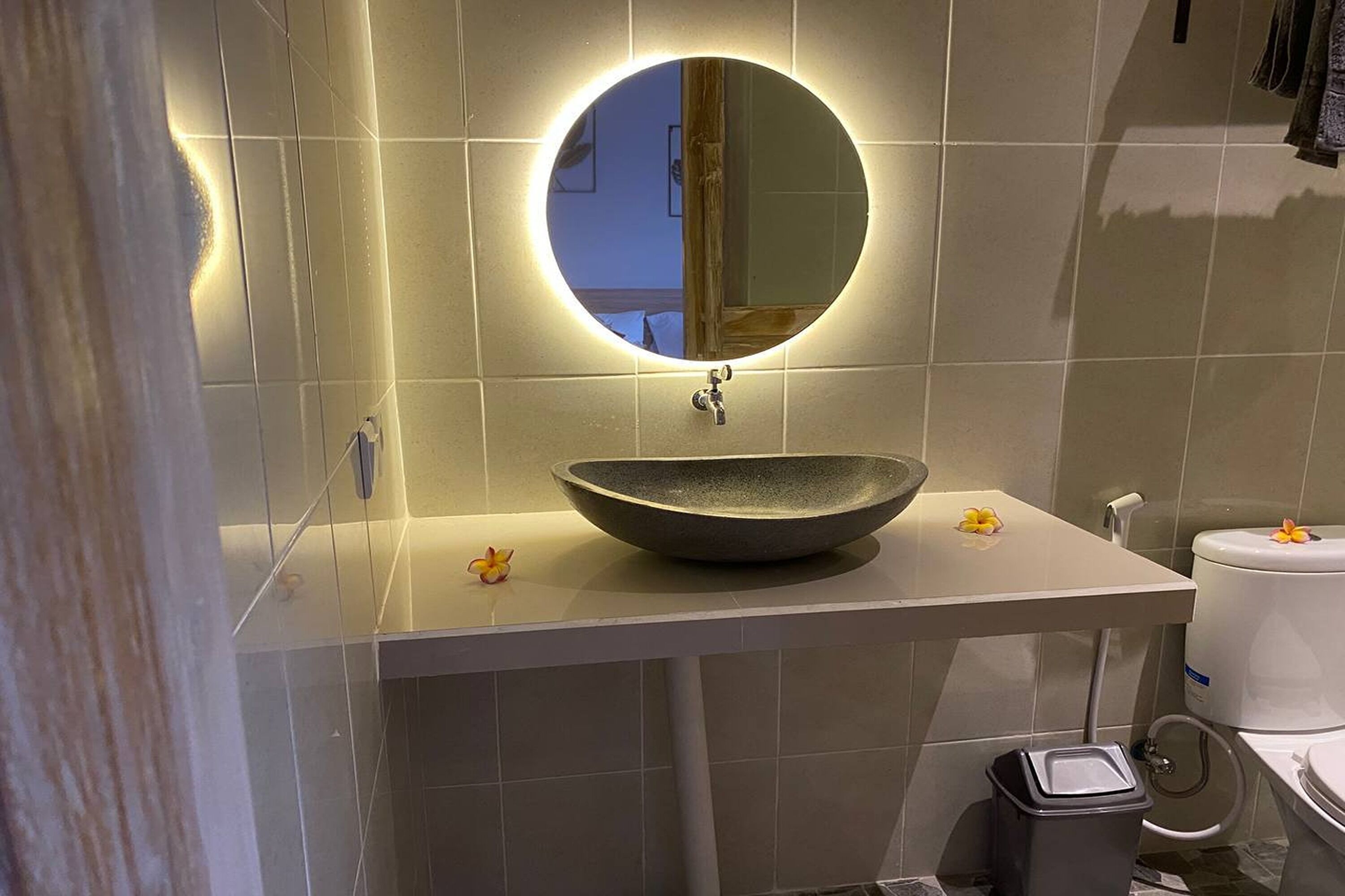 A bathroom with a round mirror, a bowl sink, and a toilet.
