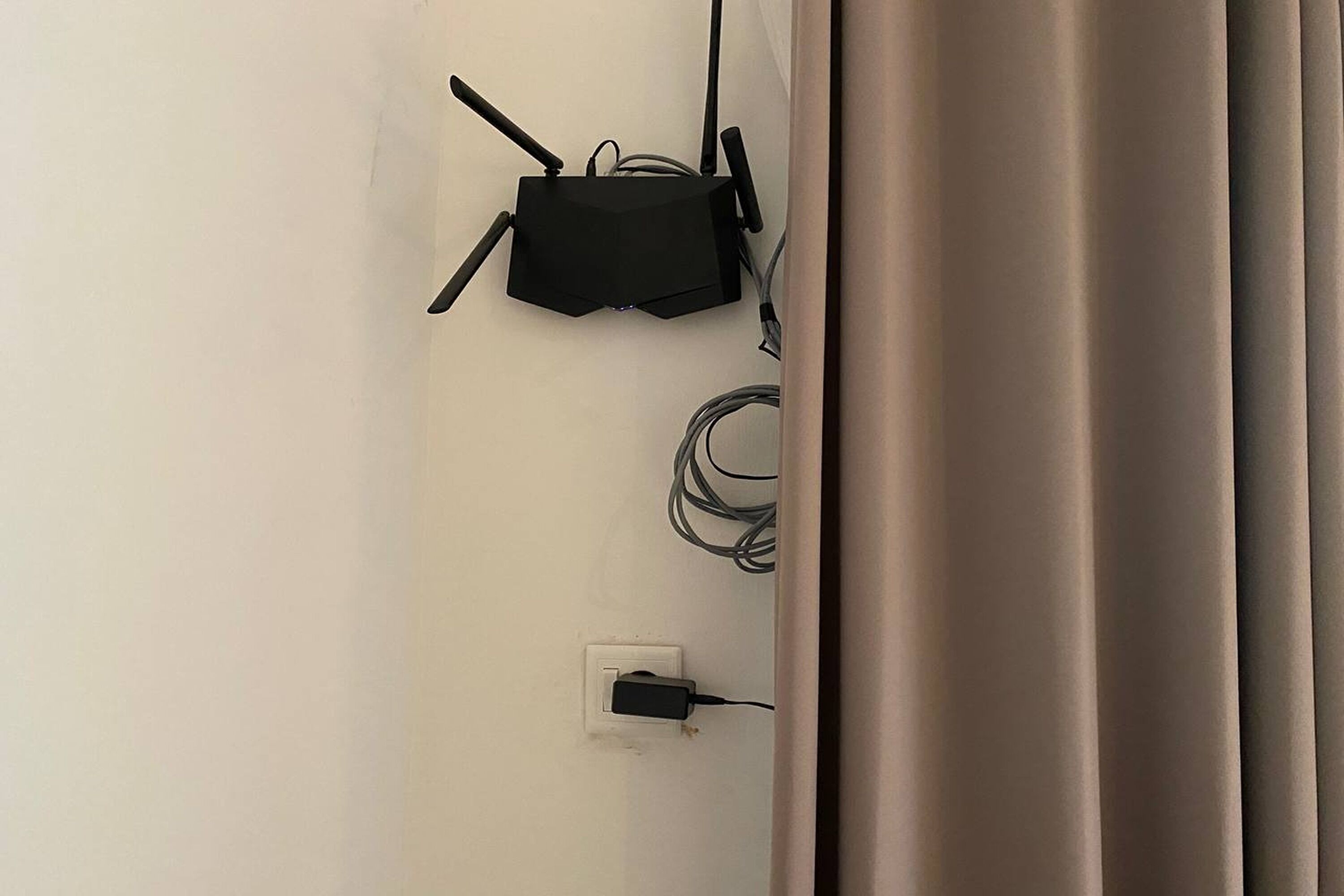 A wall-mounted router with multiple antennas and a power cord plugged into a wall socket.