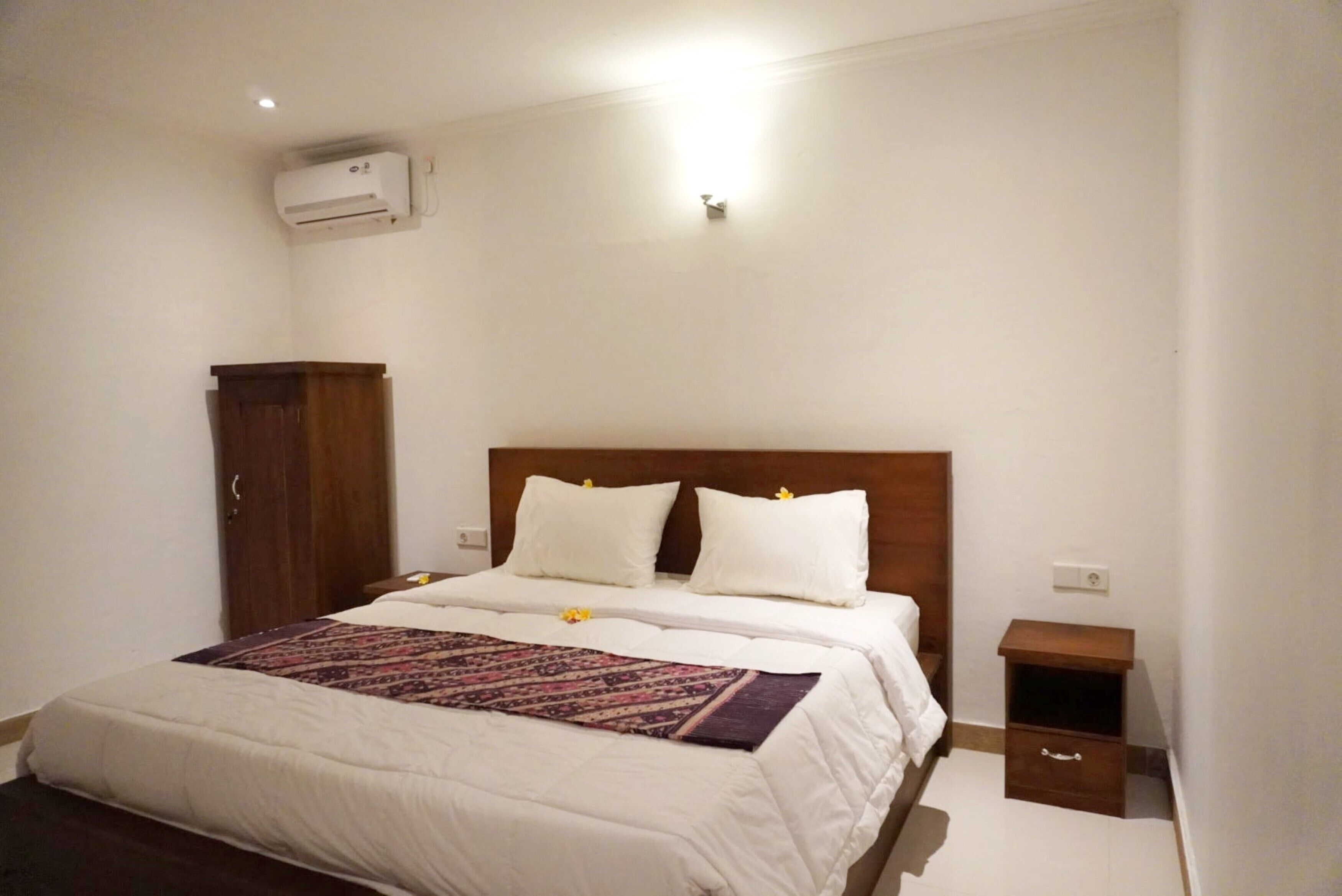 A bedroom with a bed, a nightstand, a wardrobe, and an air conditioning unit.