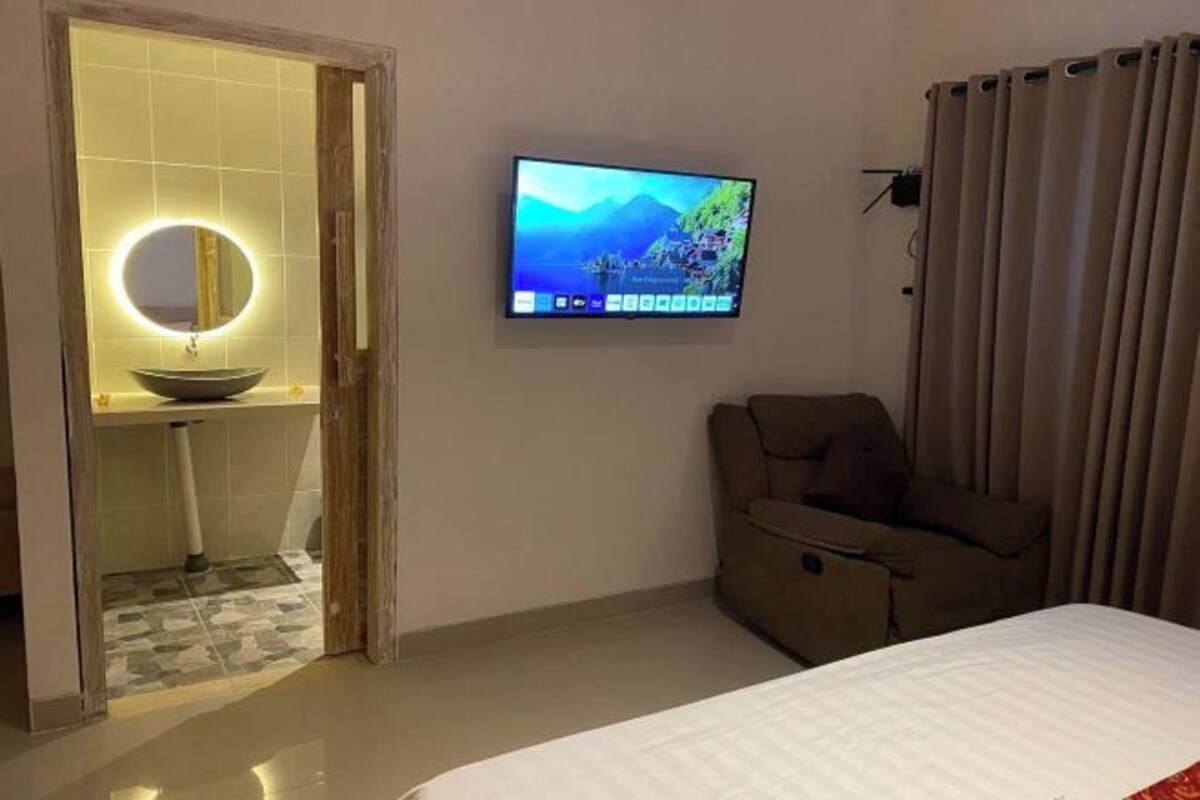 Une chambre d’hôtel comprenant un lit, un téléviseur fixé au mur, un canapé et une salle de bain avec un miroir rond et un lavabo.