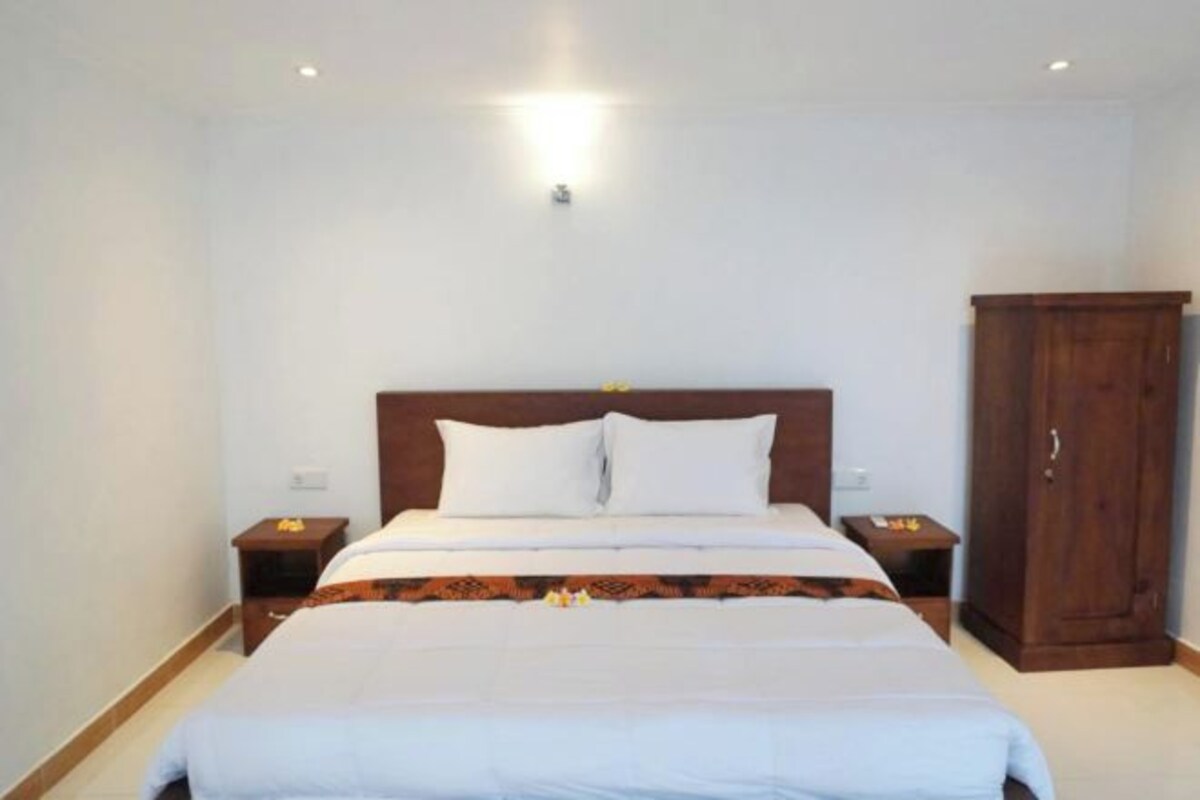 Une chambre d’hôtel avec un lit, des tables de chevet, une armoire et un luminaire au plafond.