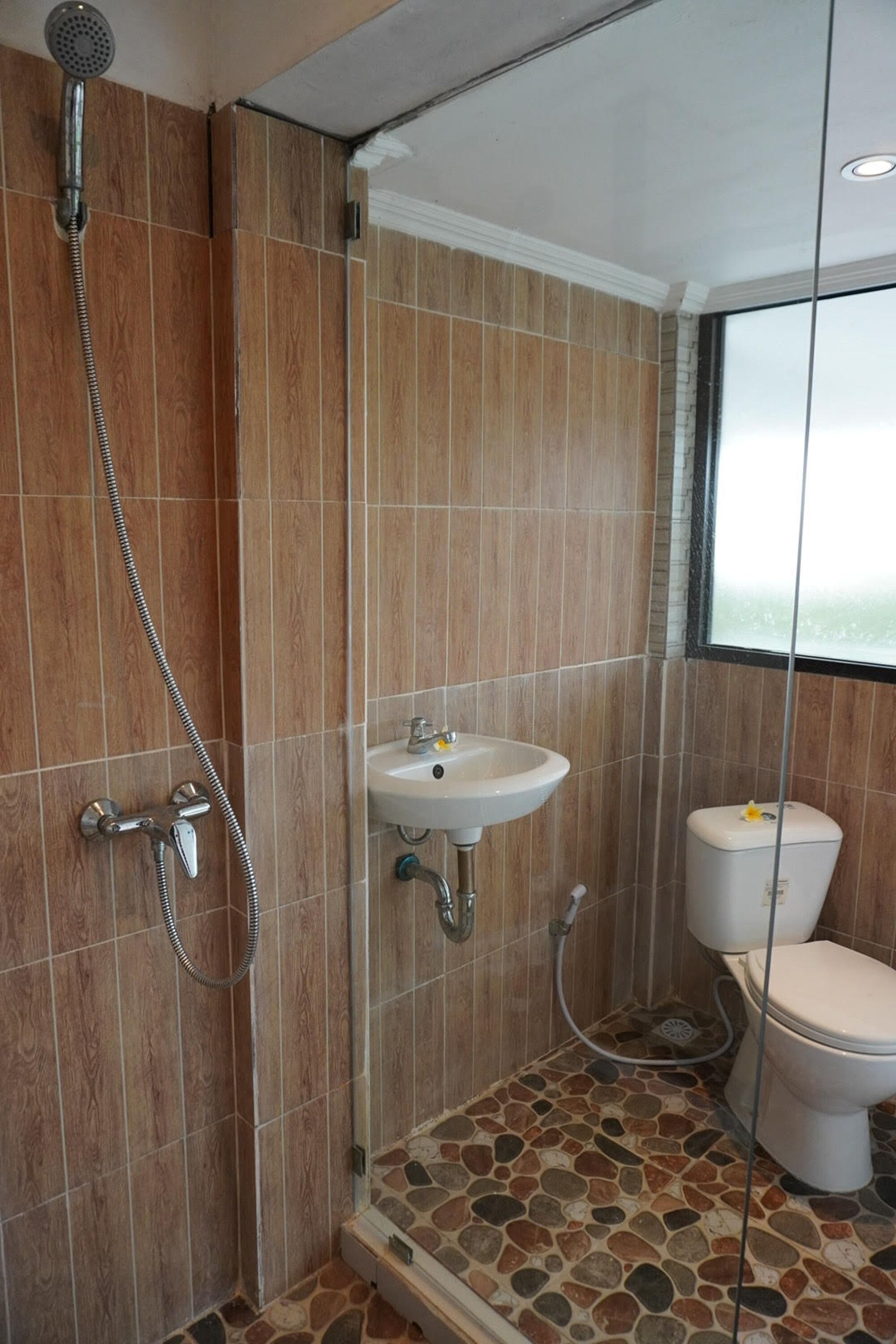 A bathroom with a shower, sink, and toilet, featuring wooden and stone tiles.