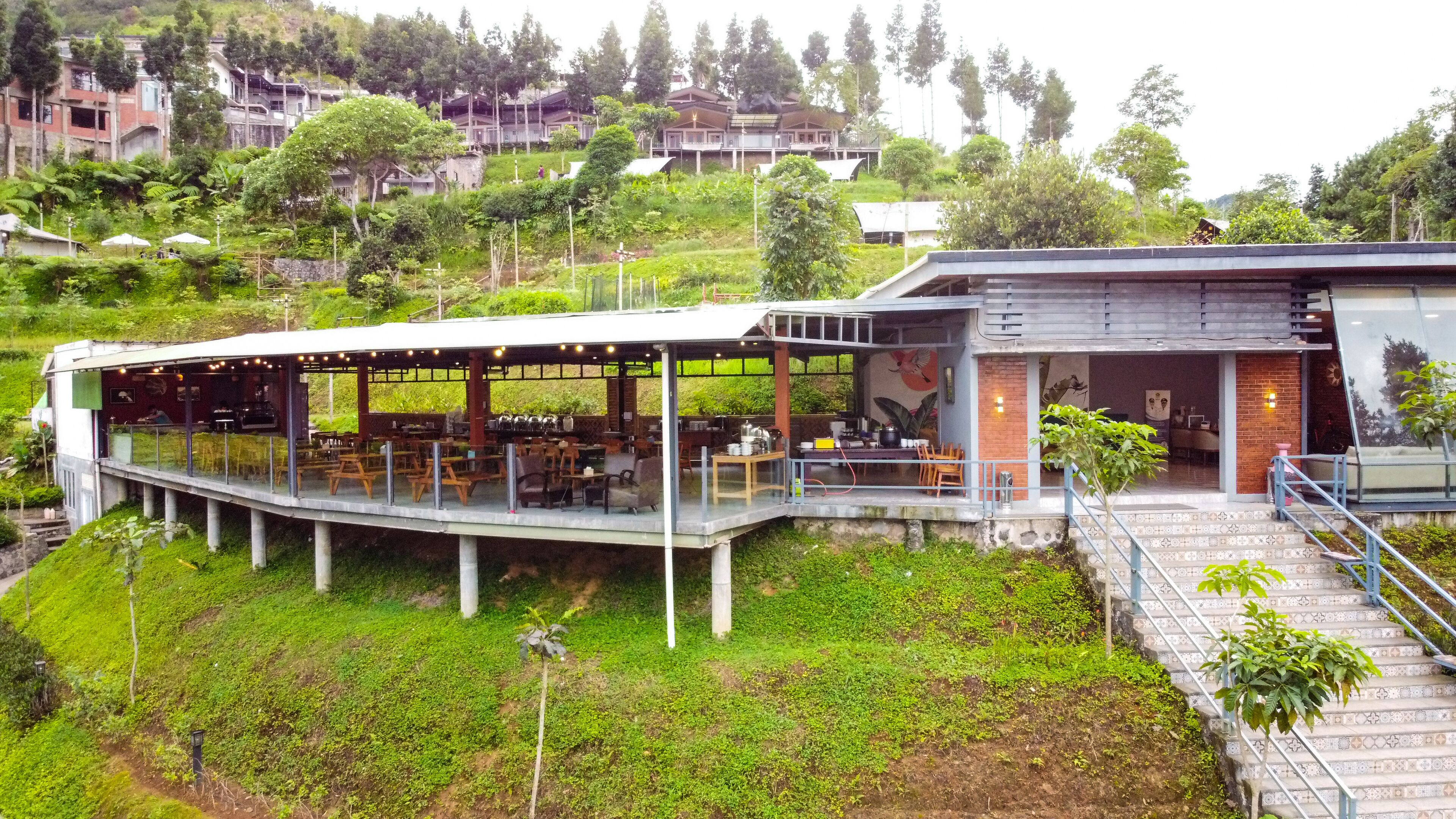 A restaurant with an outdoor seating area, a covered walkway, and a view of a hillside with buildings.
