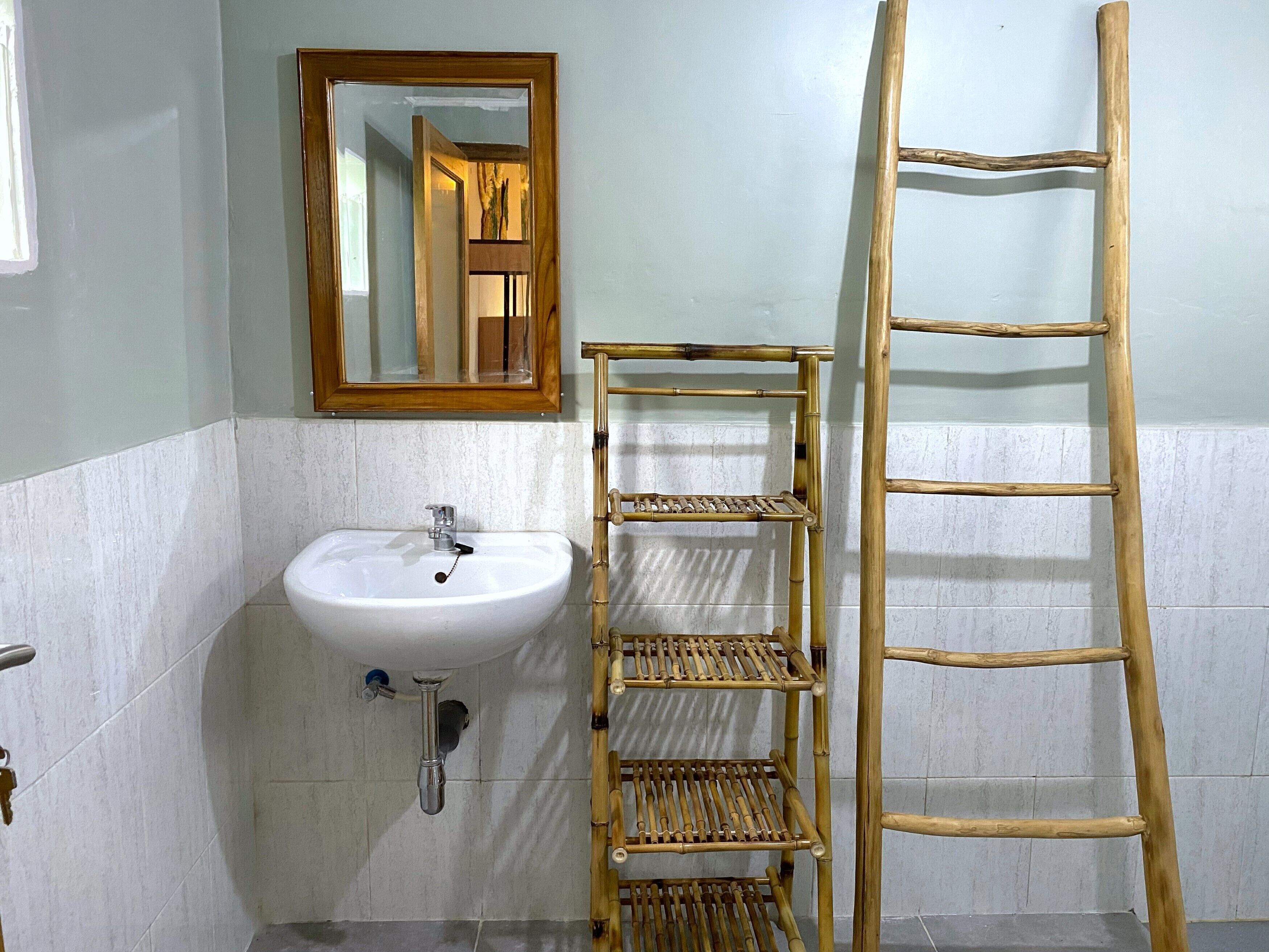 Un baño con lavamanos blanco, espejo y estante de bambú.