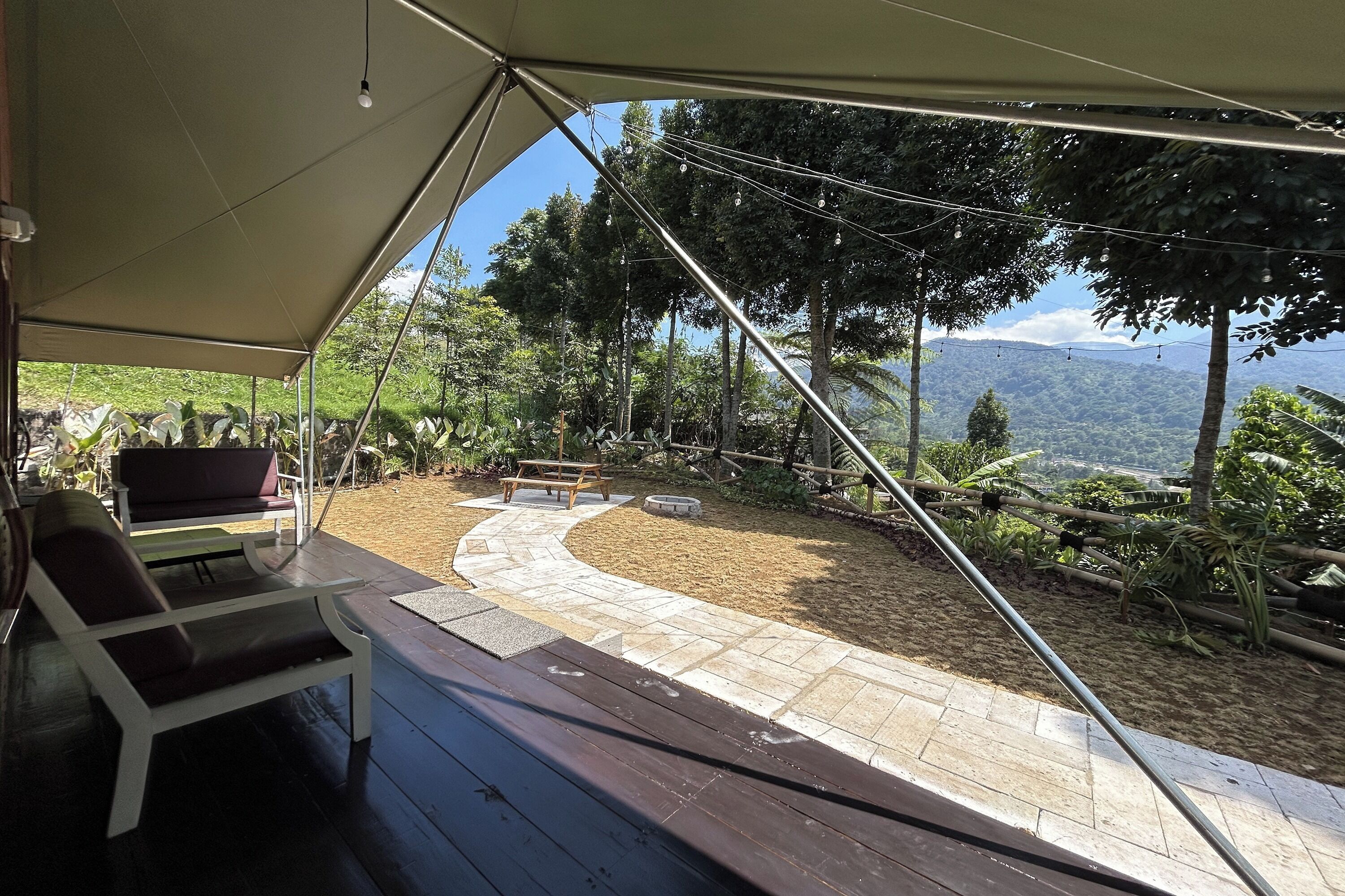 A covered outdoor area with a wooden bench, a lounge chair, and a paved pathway leading to a scenic view.