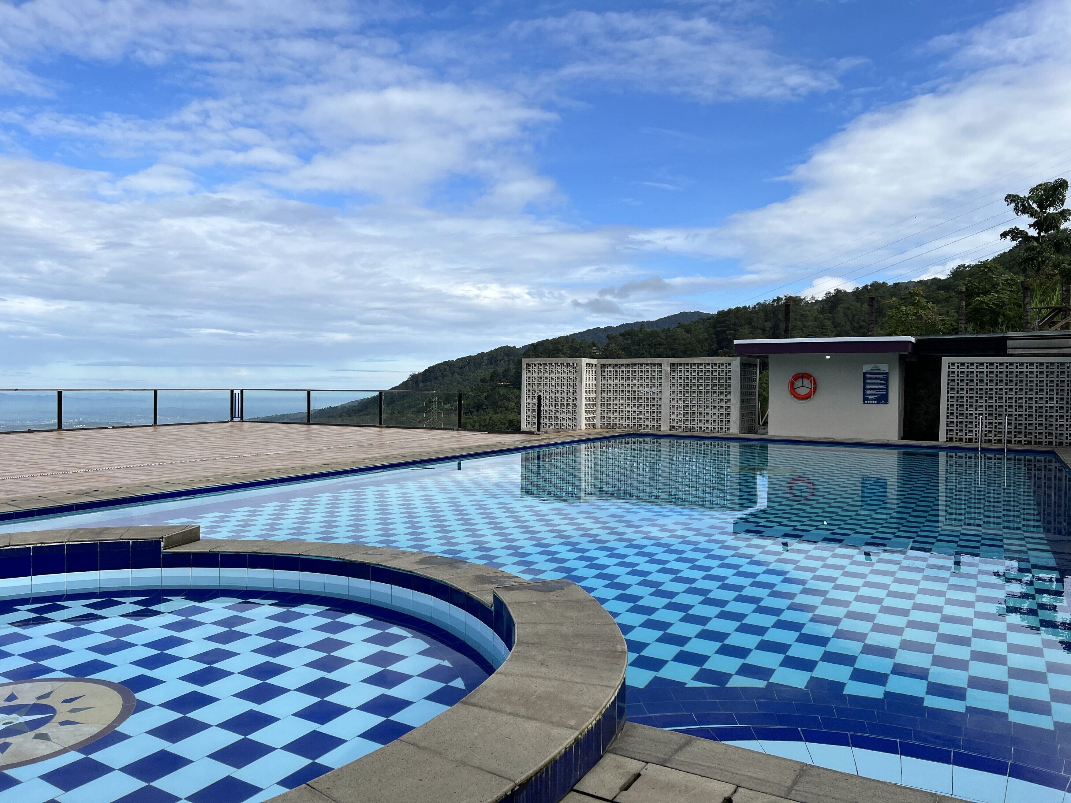 Una piscina con diseño de cuadros, rodeada por una terraza de madera y vista a un paisaje montañoso.
