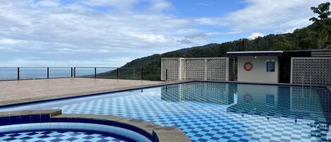 Una piscina con diseño de cuadros, rodeada por una terraza de madera y vista a un paisaje montañoso.