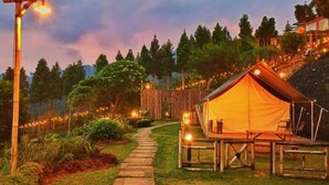 Acomodação em tenda com deck de madeira, cercada por um caminho de jardim e luzes de cordão.