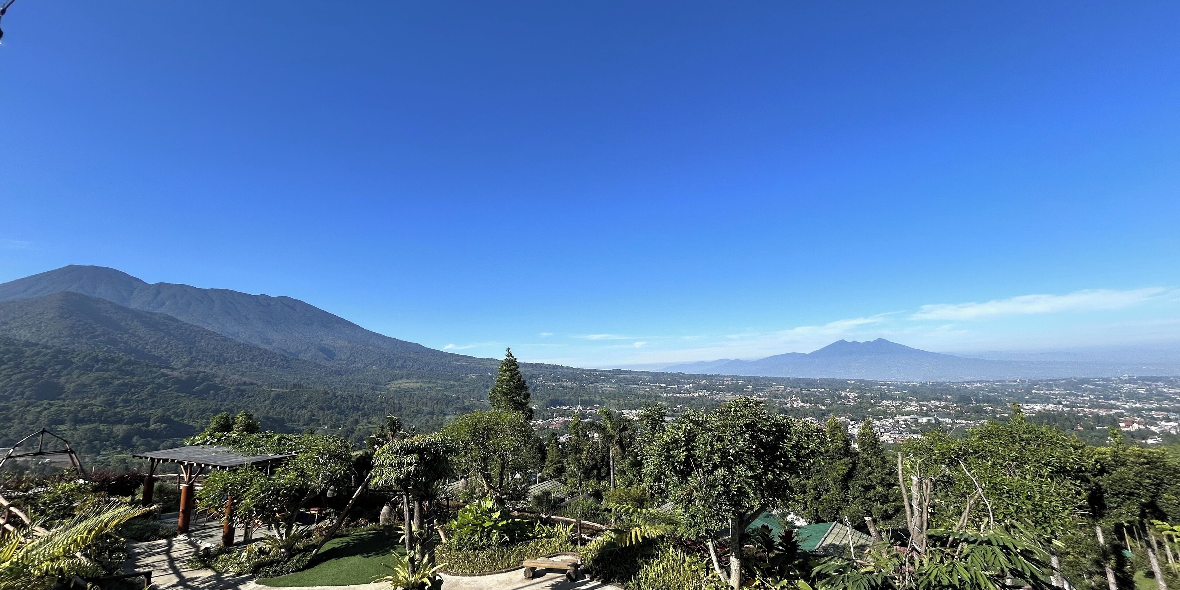 Un paisaje montañoso con cielo despejado, vista de un pueblo a lo lejos y un pabellón en primer plano.