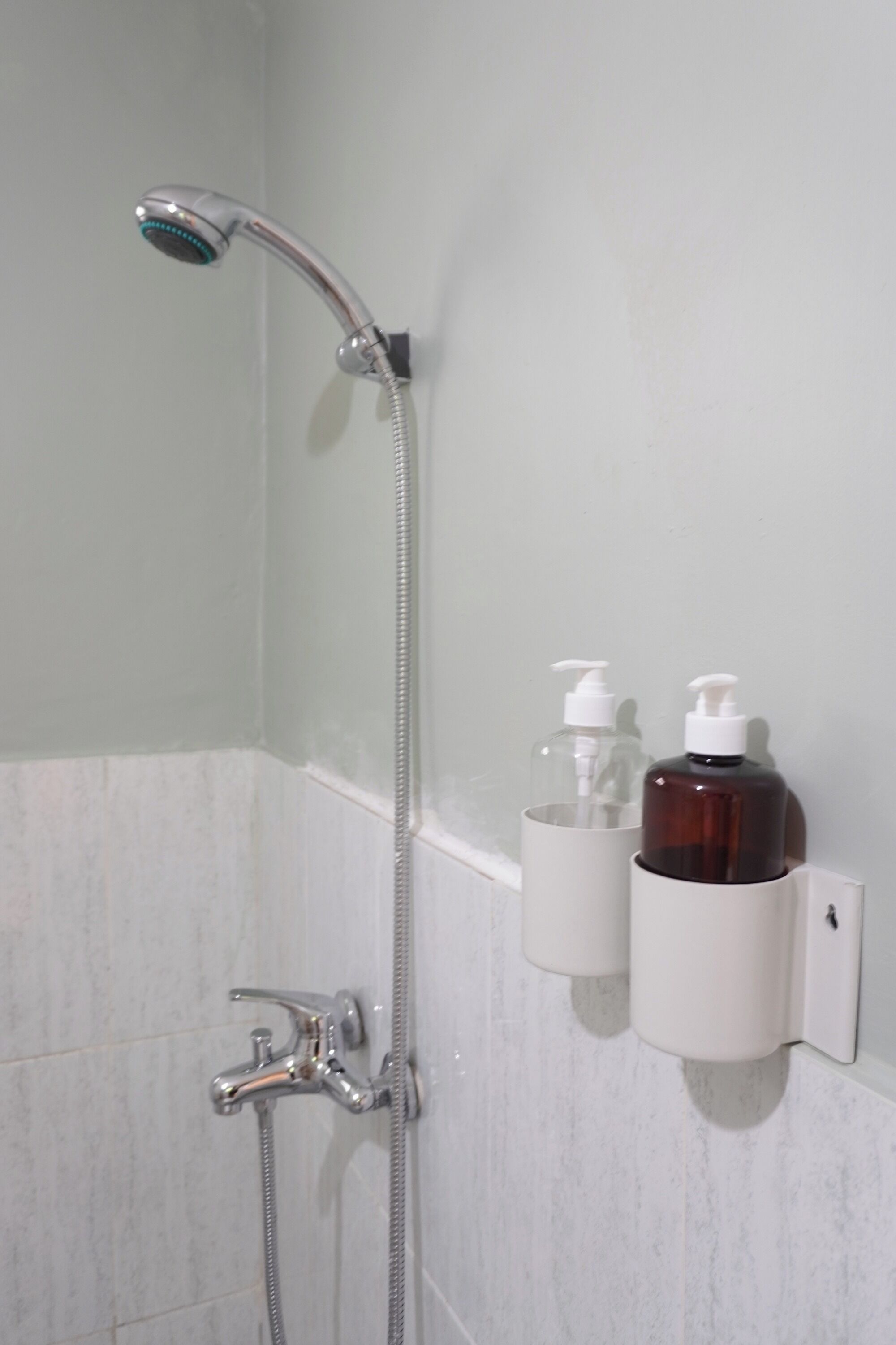 A shower with a handheld showerhead and a wall-mounted faucet. There are two soap dispensers on the wall.