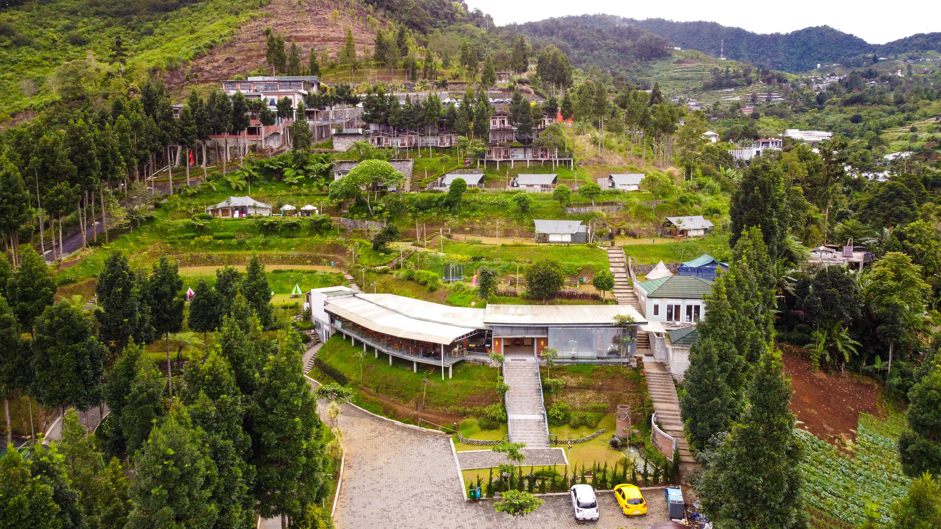 Un complejo turístico en una ladera con varias edificaciones, una estructura central con un amplio alero y un estacionamiento con varios automóviles.