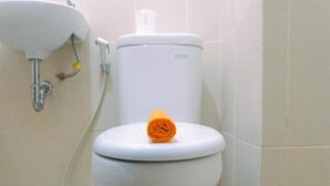 A toilet with a white seat and tank, a roll of toilet paper on the tank, and a yellow pipe connected to the wall.