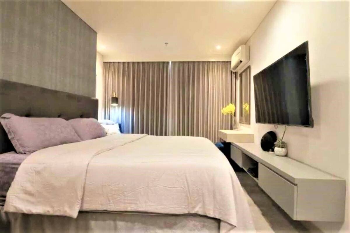Un dormitorio moderno con una cama, un televisor montado en la pared y una mesita de noche.