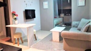 Una sala de estar moderna con un sofá, una mesita, un televisor montado en la pared y una ventana con vistas.
