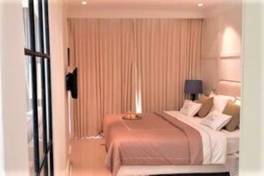 Et hotelværelse med en seng, et natbord, en lampe og et gardin.