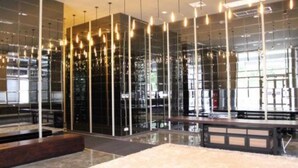Un interior moderno con paredes de vidrio reflectante, lámparas colgantes y una zona de estar central.