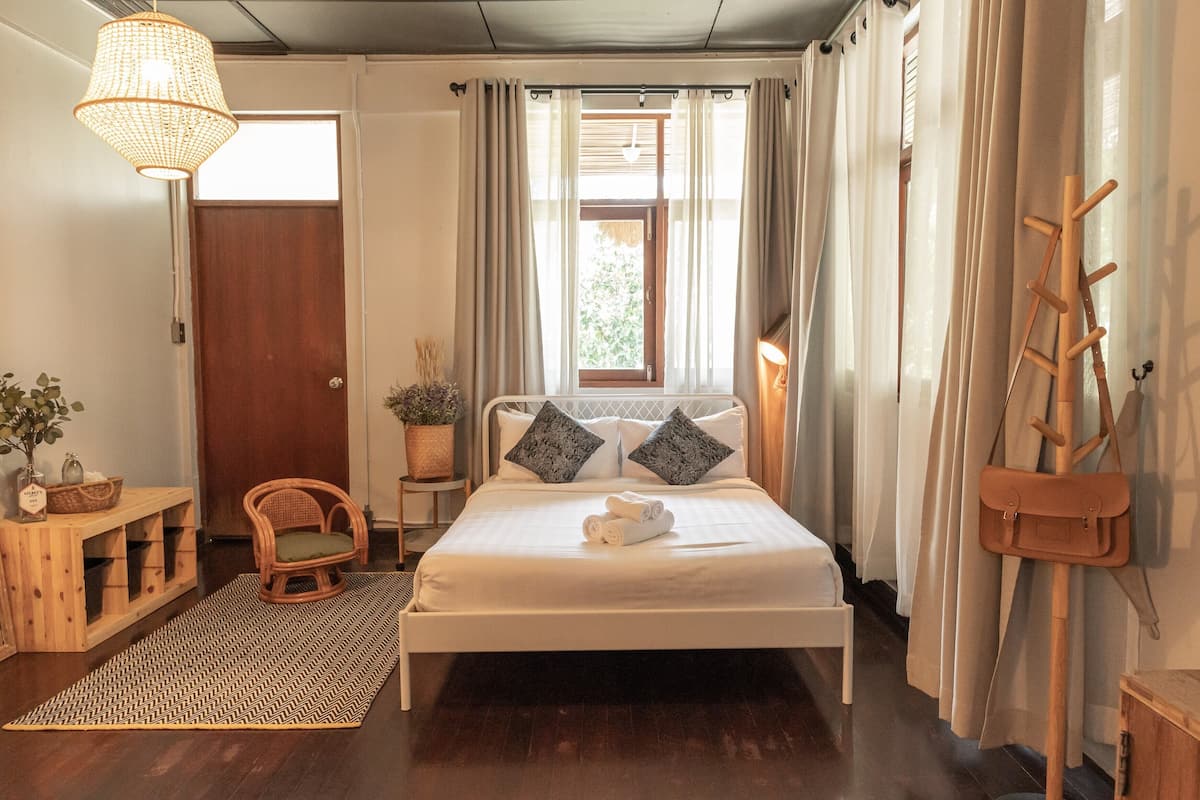 A neatly arranged bedroom with a bed, a chair, a small table, and a hanging coat rack.