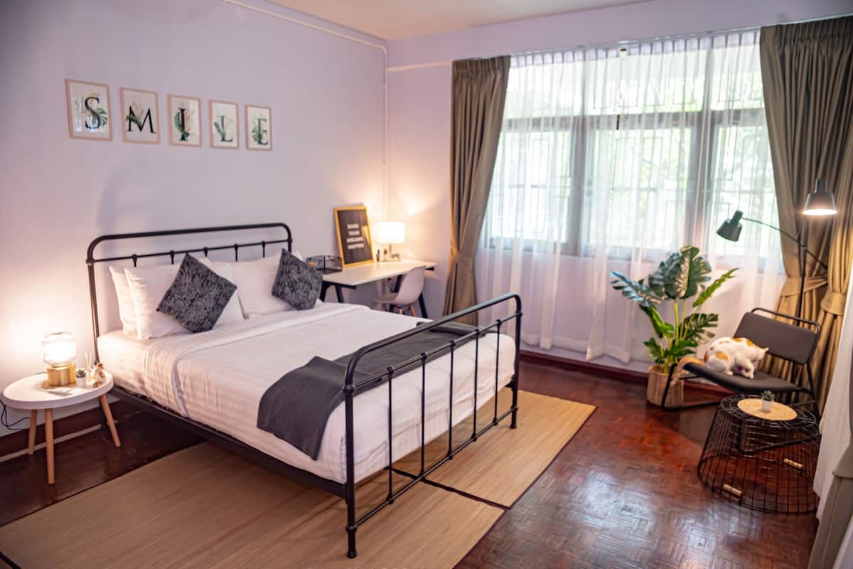 A neatly arranged bedroom with a bed, bedside table, lamp, and a desk with a chair.