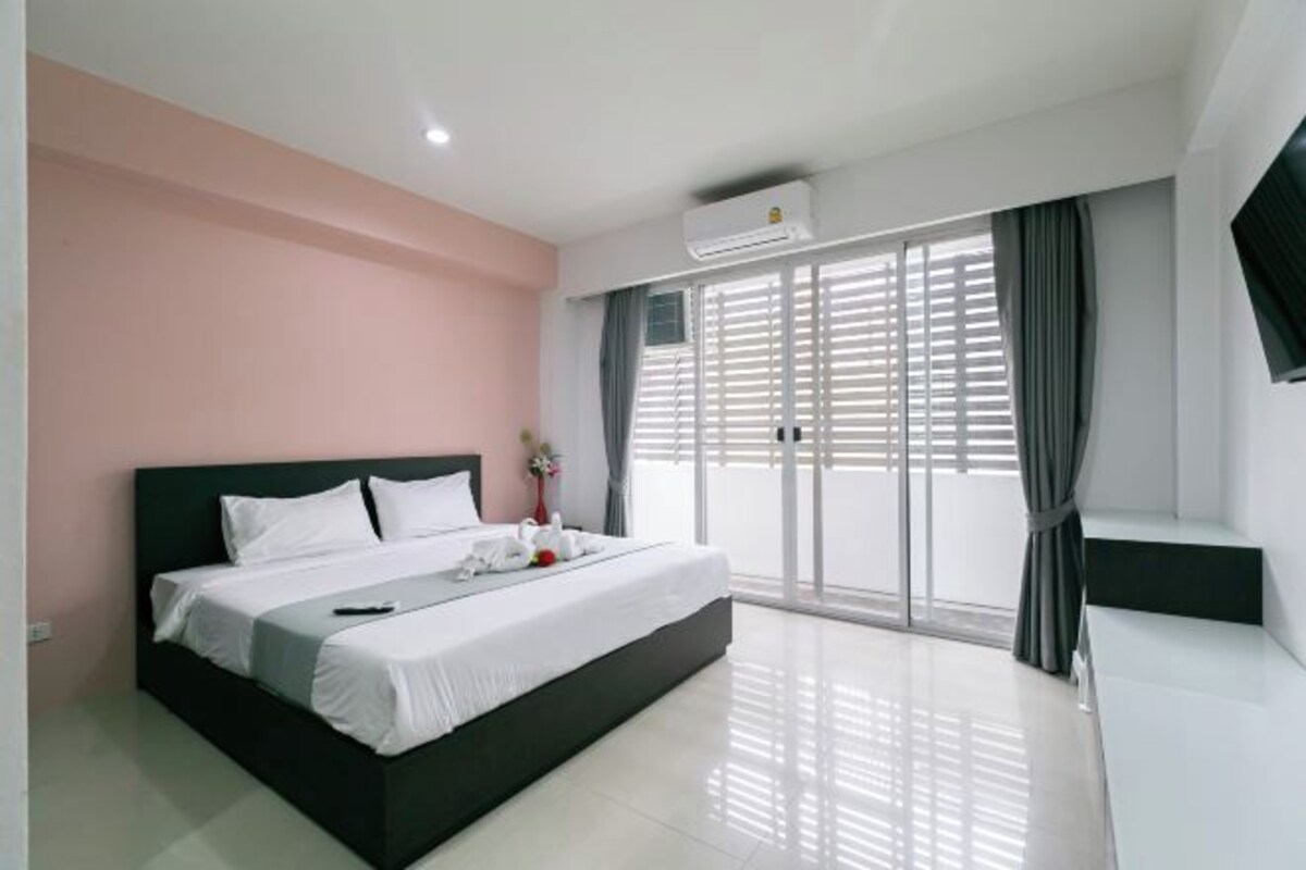 Un dormitorio moderno con una cama grande, un ventanal corredizo a un balcón y un televisor de pantalla plana en la pared.