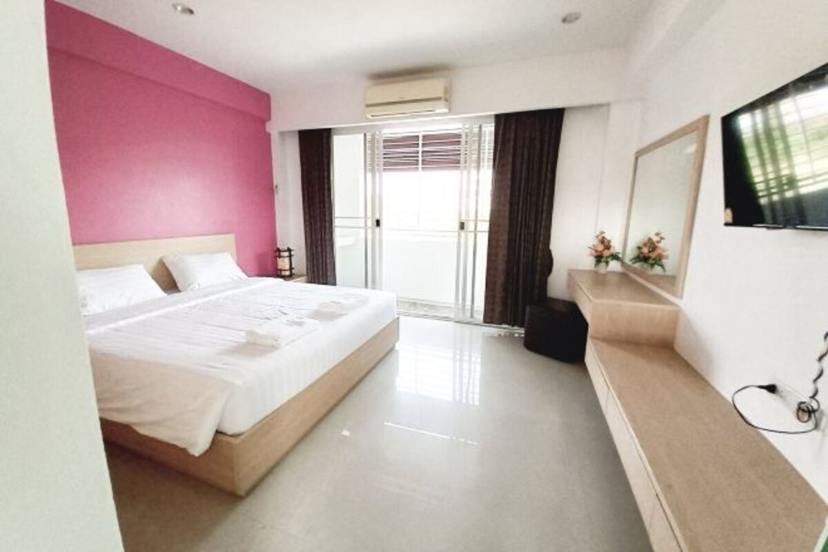 Una habitación de hotel con cama, televisor, escritorio y un ventanal con cortinas.