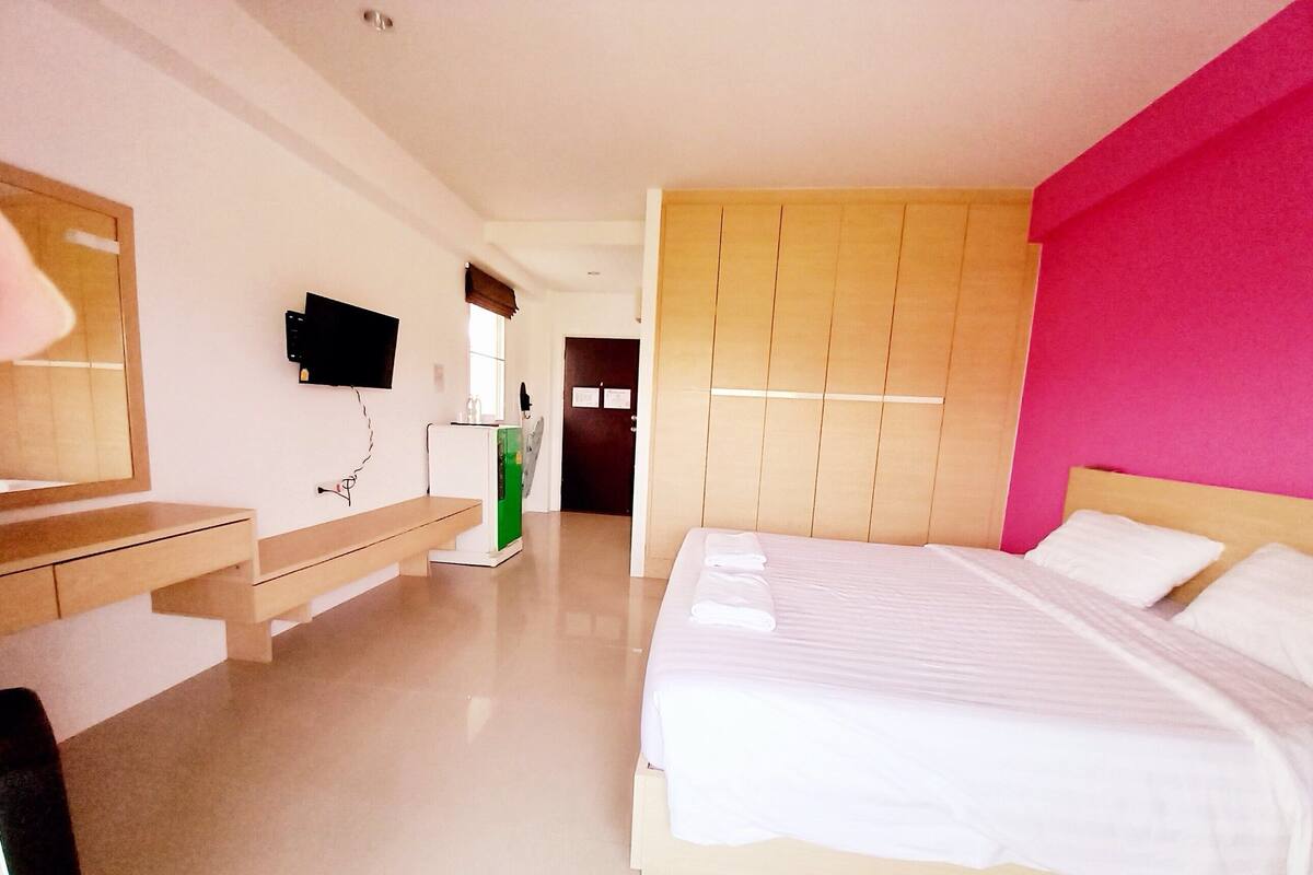 Une chambre d’hôtel équipée d’un lit, d’un bureau, d’un miroir, d’une télévision et d’une porte donnant sur une autre pièce.