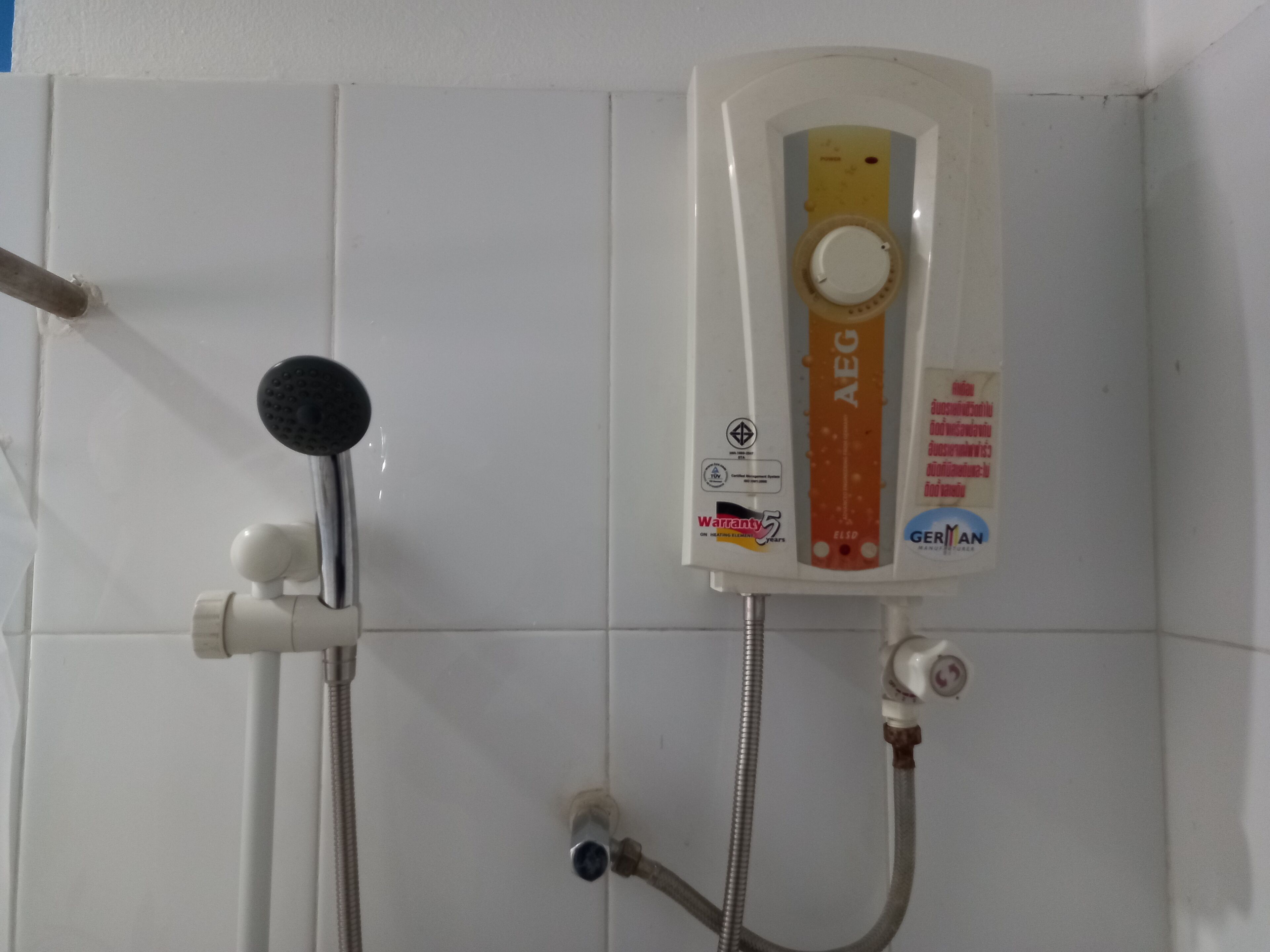 A wall-mounted shower unit with a control panel, a handheld showerhead, and a flexible hose.