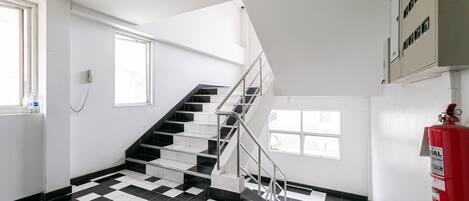 A staircase with a metal handrail, a fire extinguisher mounted on the wall, and a checkered floor pattern.