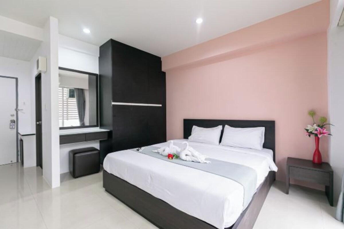 A modern hotel room with a large bed, a bedside table with a vase of flowers, and a mirror above the desk.