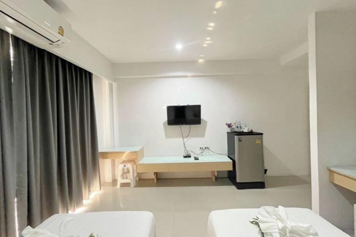 Una habitación de hotel con dos camas, un escritorio, un televisor montado en la pared y un minibar.