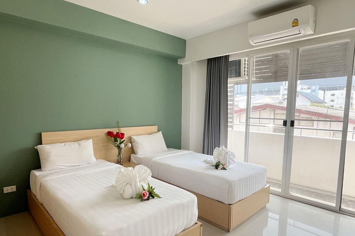 Une chambre d’hôtel avec deux lits, un mur vert, une grande fenêtre donnant sur un beau paysage et un appareil de climatisation.