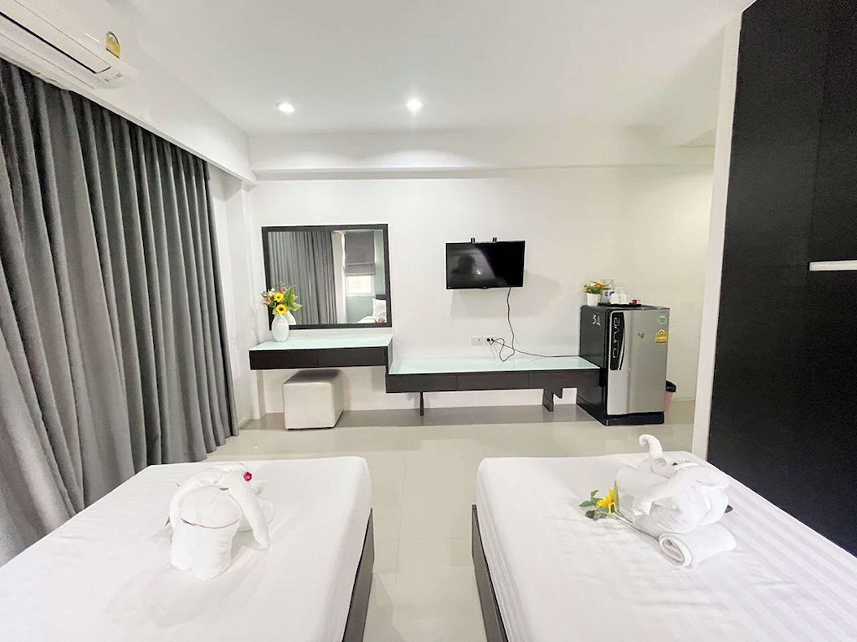 A hotel room with two beds, a desk with a mirror, a television, and a minibar.