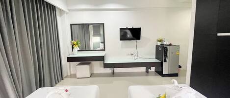 A hotel room with two beds, a desk with a mirror, a television, and a minibar.