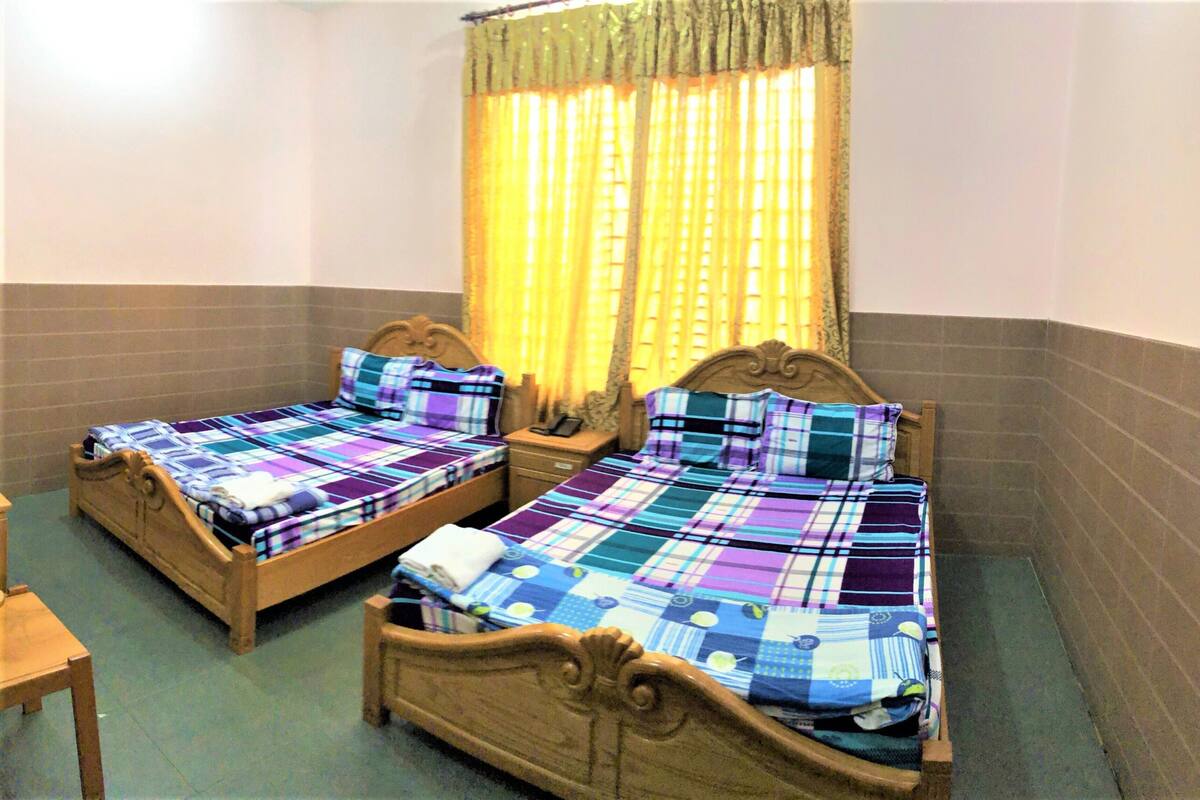 Two wooden beds with plaid bedding, a wooden nightstand, and a window with yellow curtains.
