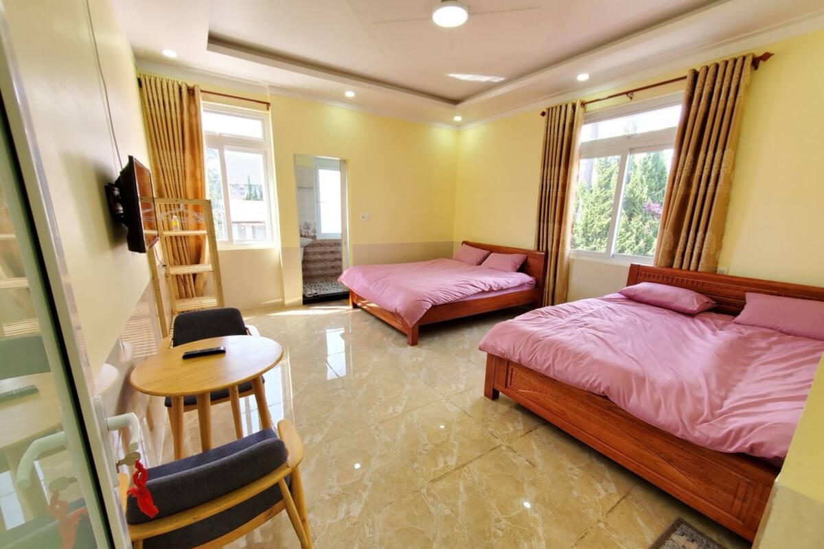 A hotel room with two beds, a small table, a chair, a TV, and a window with curtains.