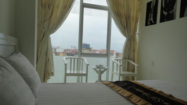 A hotel room with a bed, a small table, two chairs, and a view of the city through a large window. - SIC Hotel (Dong Hoi)