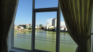 A room with a large window overlooking a river and buildings. - SIC Hotel (Dong Hoi)