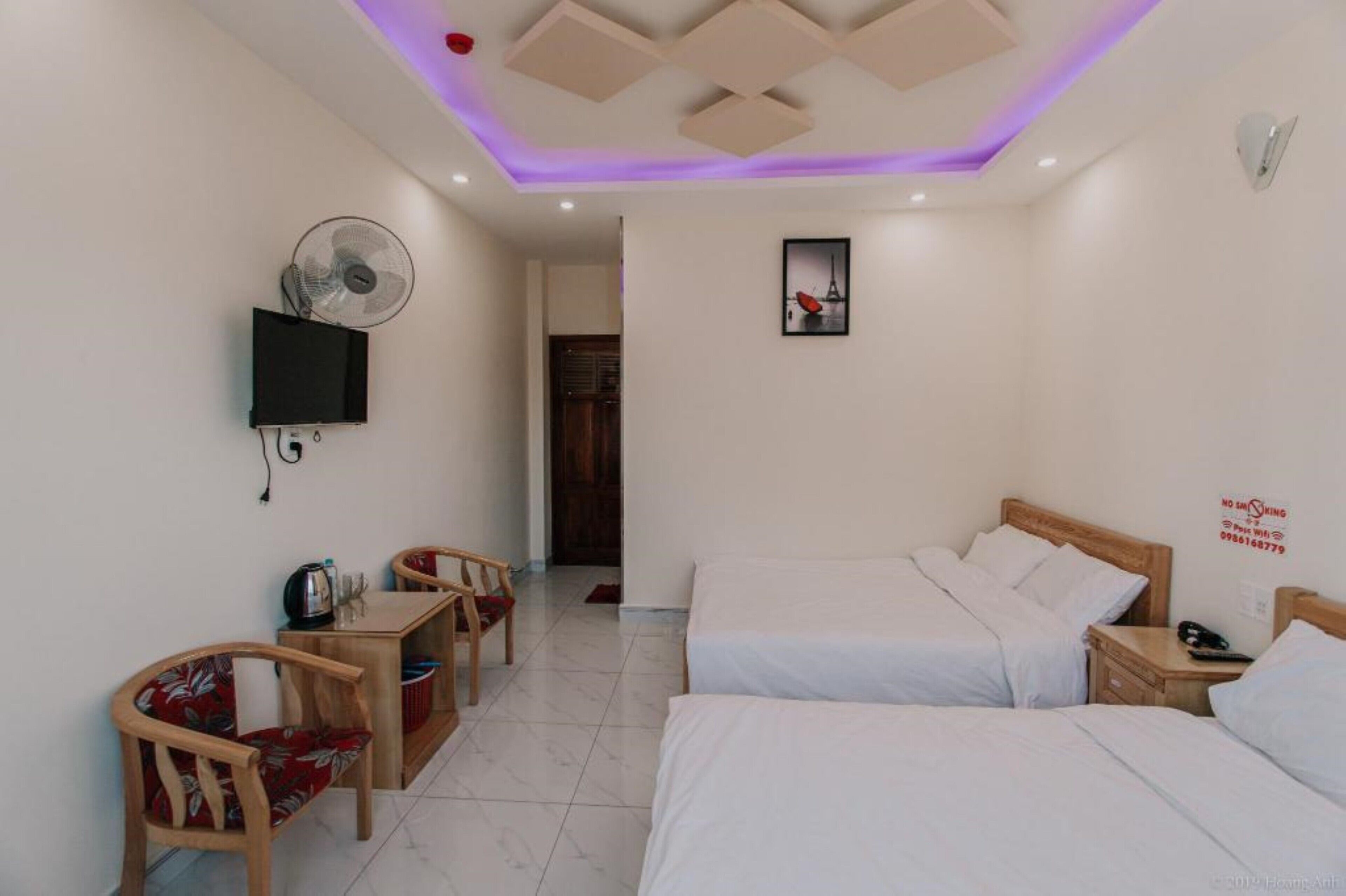 Ein Hotelzimmer mit zwei Betten, einem Schreibtisch mit Stuhl, einem Wand-Fernseher und einem Deckenventilator.