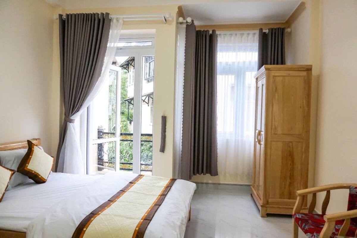 A bedroom with a bed, curtains, a wooden wardrobe, and a chair.