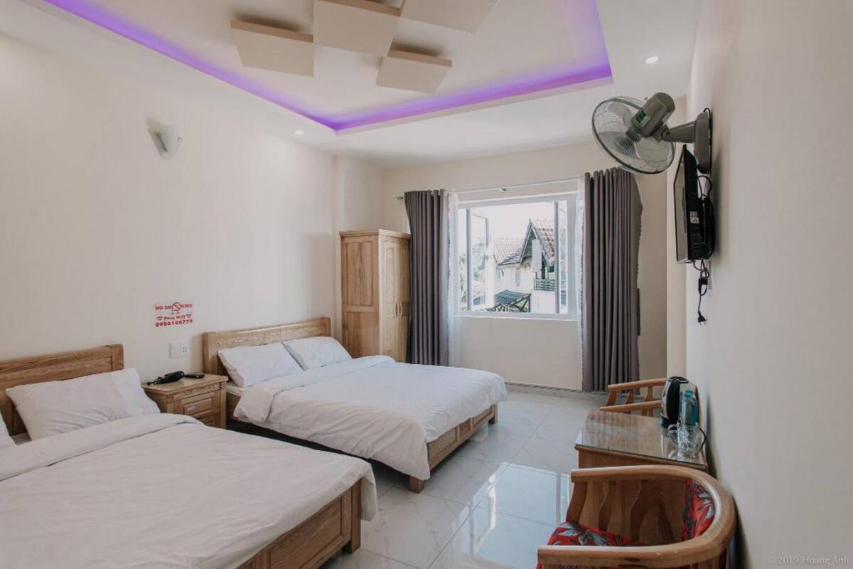 A hotel room with two beds, a TV, a fan, and a window with curtains.