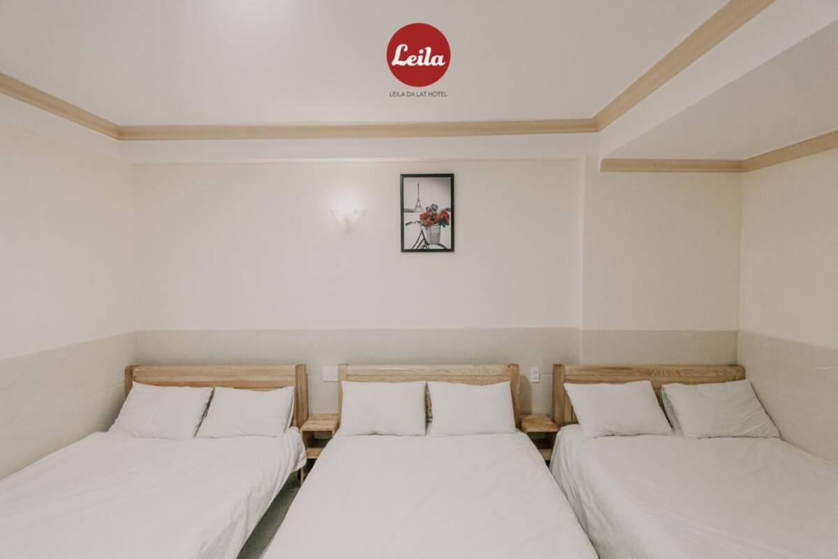 A hotel room with three single beds, a framed picture on the wall, and a logo above the beds.