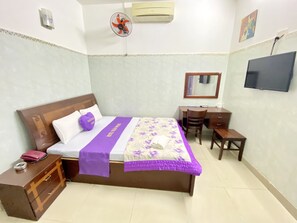 Een keurig opgemaakt slaapkamer met een bed, een bureau, een stoel, een dressoir en een televisie die aan de muur is bevestigd.