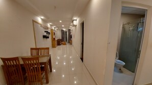 A hallway with a dining area featuring a table and chairs, a glass-enclosed shower, and a door leading to another room. - Gianni Hotel (Ho Chi Minh City)