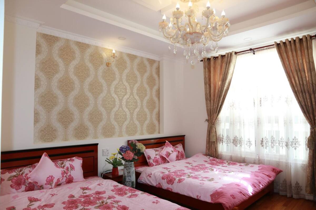 Camera d'albergo con due letti, biancheria da letto floreale, un lampadario e carta da parati decorata.