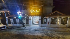 Entrada de hotel com letreiro de neon, portão e um carro branco estacionado na frente.