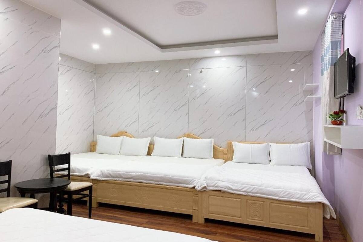 Une chambre d’hôtel avec deux lits, une tête de lit en bois, un téléviseur fixé au mur et une petite table avec des chaises.