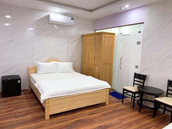 Une chambre avec un lit en bois, une armoire, une petite table avec des chaises et un appareil de climatisation.